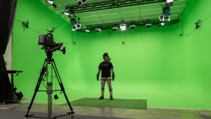 A man wearing a motion capture suit inside the green screen space of Miami Mocap Studios in front of a 8k digital video camera